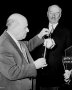 Cellist Pablo Casals shows conductor Sir Adrian Boult how to use a tiny Catalonian drum called a Sardinia as Casals' wife looks on.